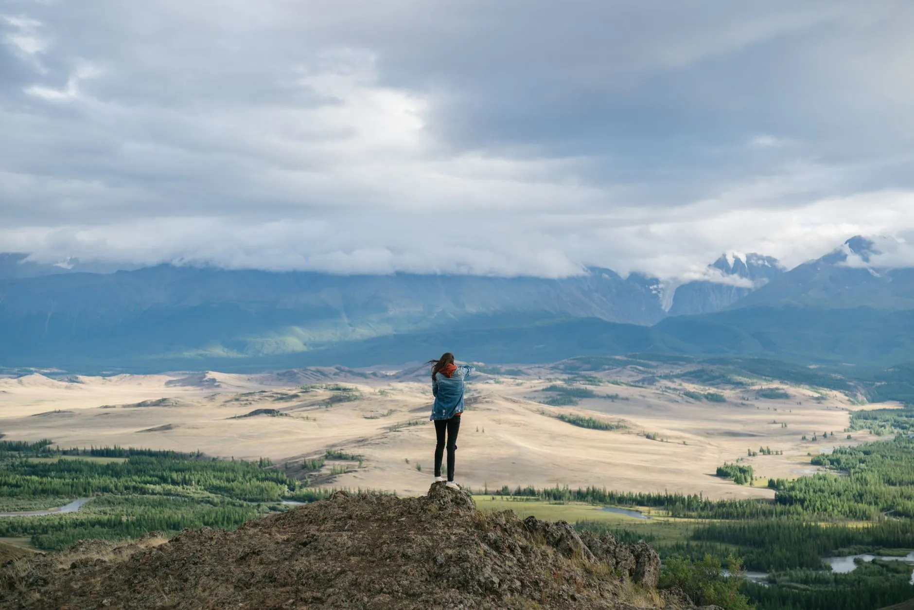 A traveller standing on a rocky peak looking over a wide mountain valley